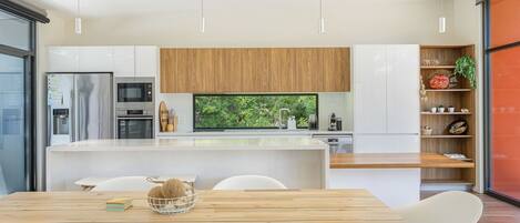 Una cocina moderna con armarios blancos, encimera de madera y vistas a zonas verdes a través del ventanal.