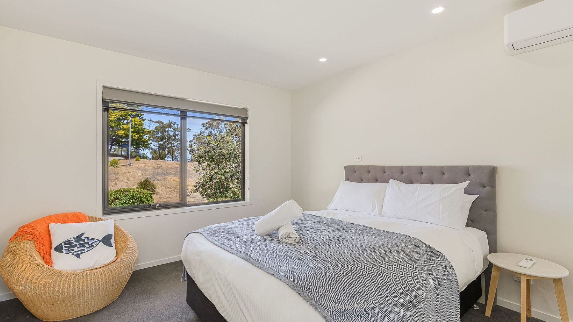 Un dormitorio con cama, una ventana que da a árboles, una silla y una mesita de noche.