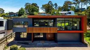 Une maison moderne à deux étages, dotée d’une grande baie vitrée au rez-de-chaussée, d’un balcon et d’un garage.