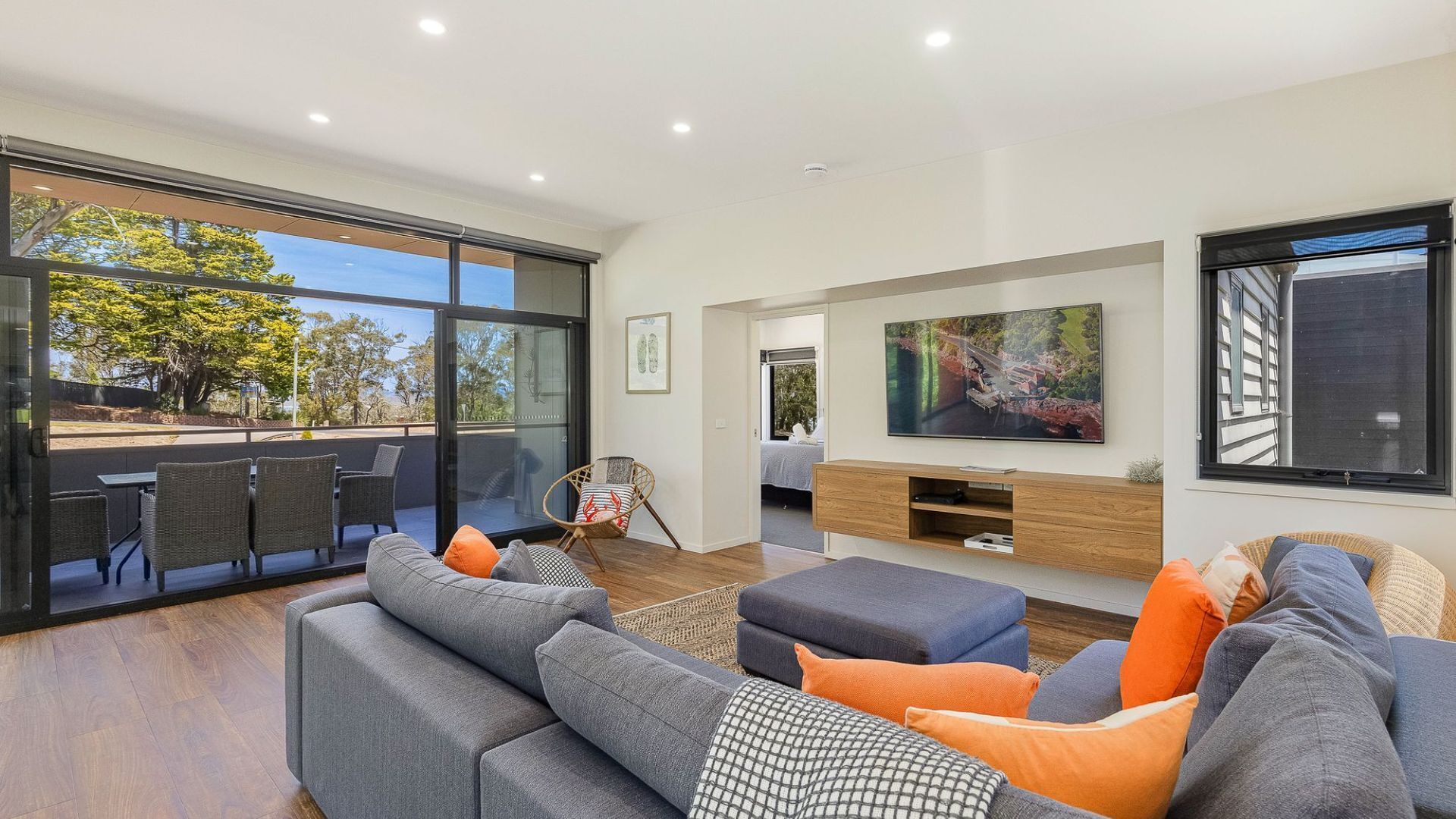 A modern living room with a large sofa, a TV, and a glass door leading to an outdoor area.