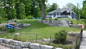 Une maison avec un mur de soutènement en pierre, une cour gazonnée et un quai.