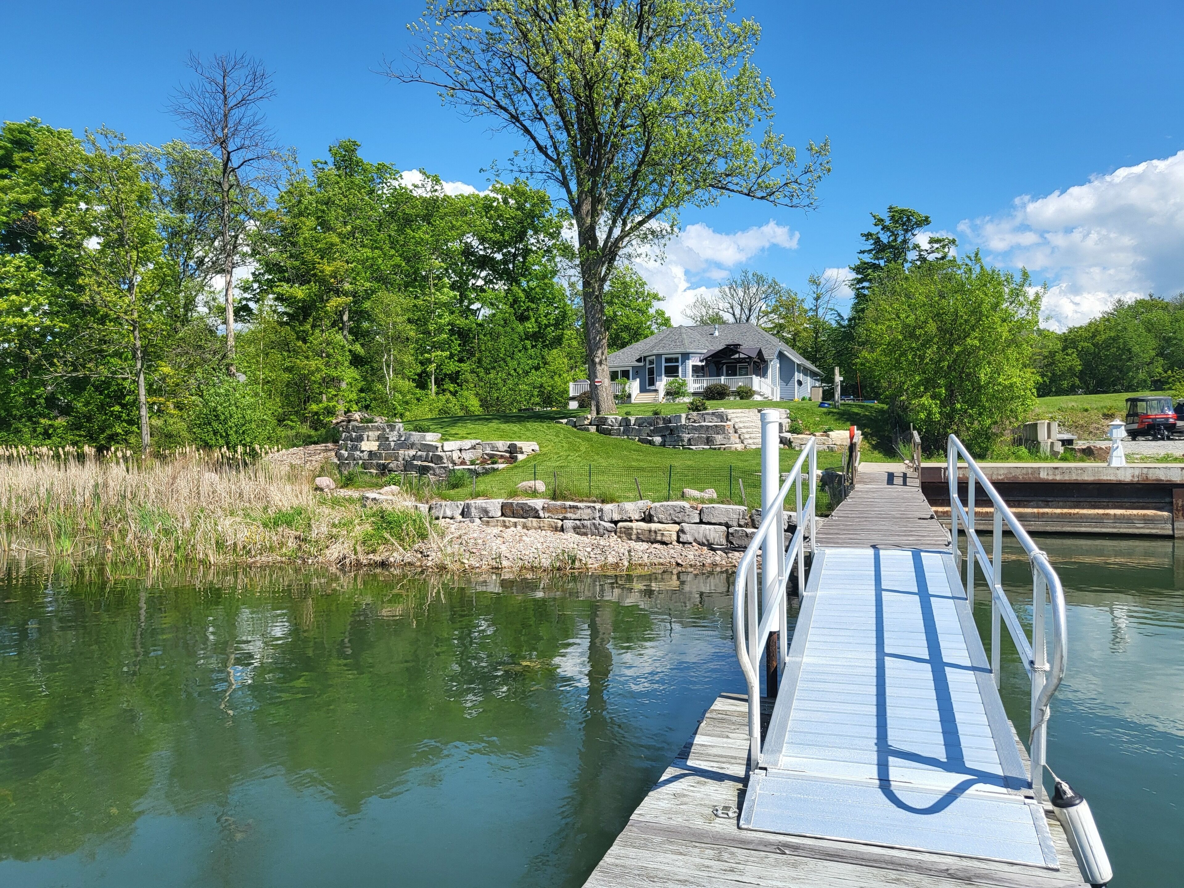 A wooden dock leading to a house with a porch, surrounded by trees and a body of water.