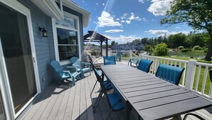 Une terrasse couverte, dotée d’une table et de chaises, qui offre une vue sur un lac et sur des maisons.