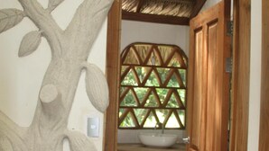 A bathroom with a wooden door, a sink, and a decorative tree sculpture.