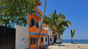 Un edificio costero con fachada azul y naranja, palmeras y vista despejada al mar.
