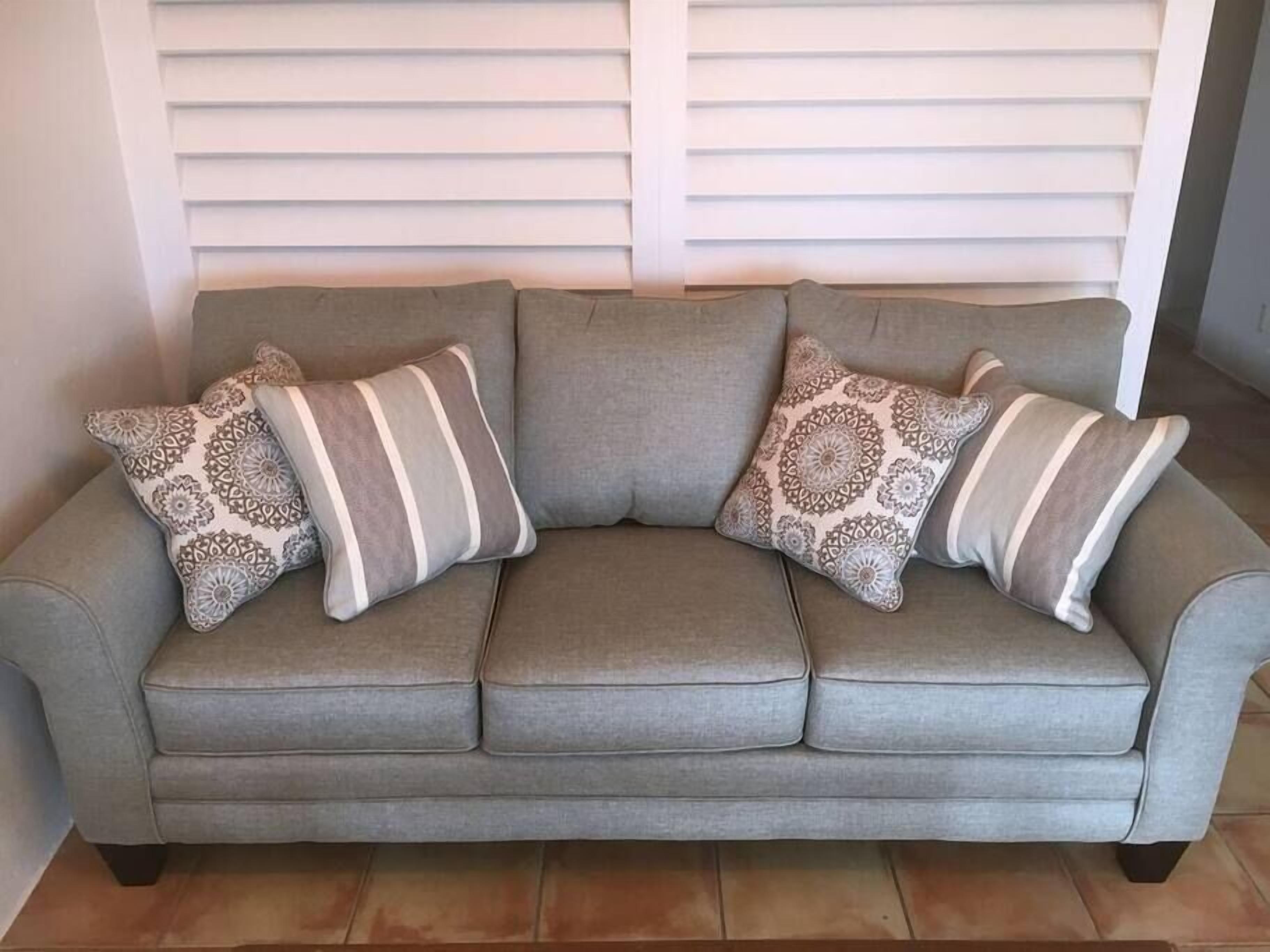 A grey sofa with four patterned cushions in a living room with white blinds in the background.