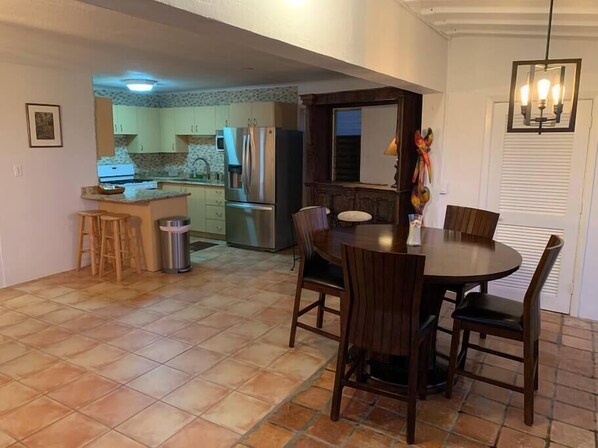 A compact kitchen with a dining area, featuring a tiled floor, stainless steel appliances, and a wooden dining table with chairs.