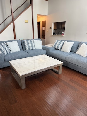 Ein Wohnzimmer mit grauem Ecksofa, einem Marmortisch und Holzböden.