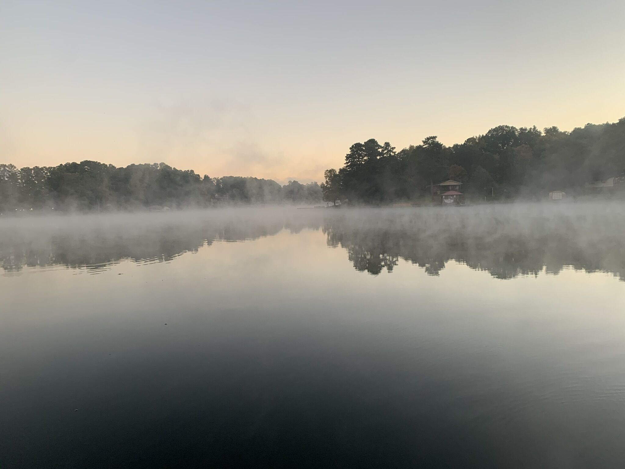 Un lac paisible où se reflètent les arbres et un bâtiment situé sur la rive opposée.