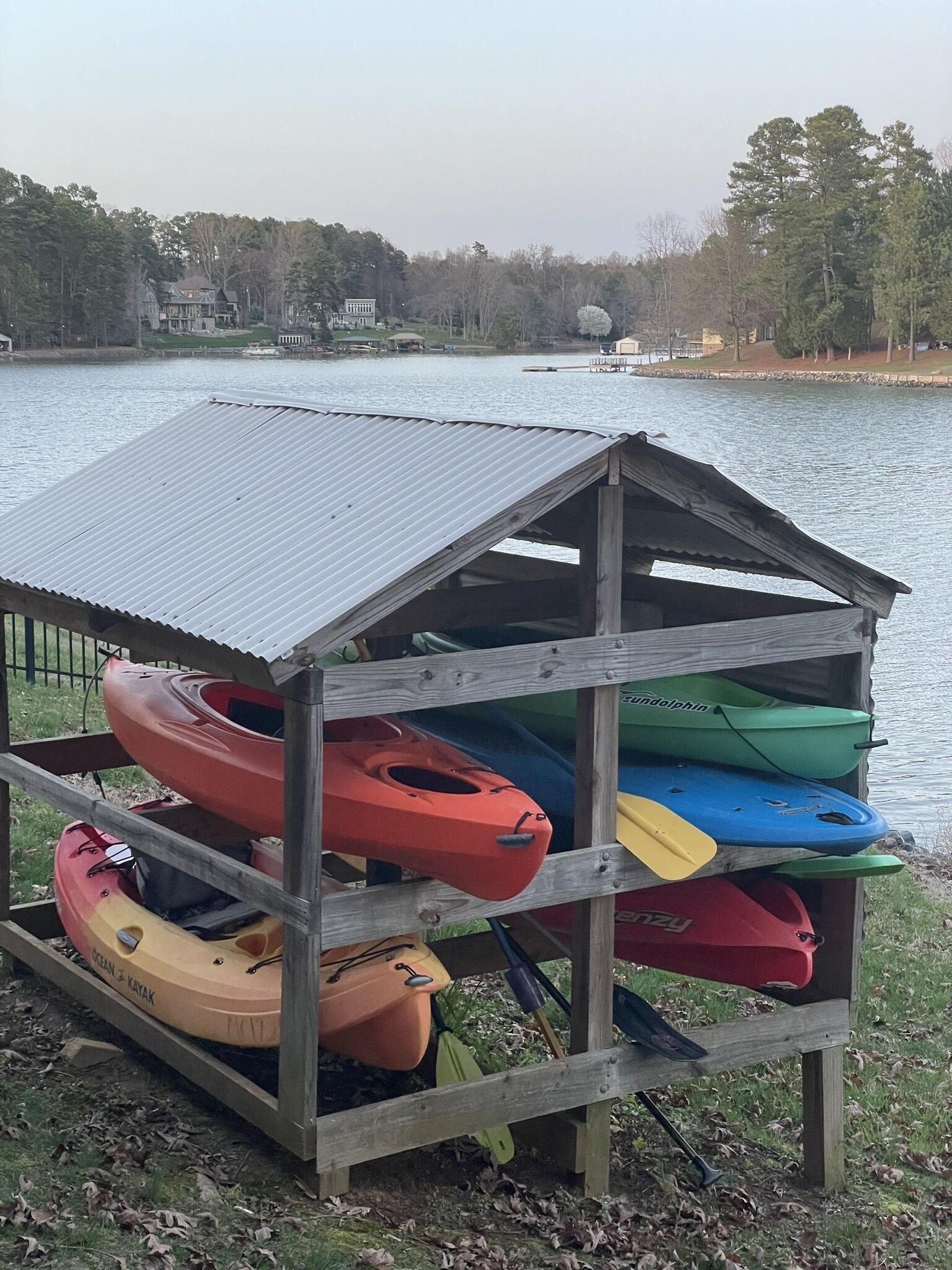 Estructura cubierta para guardar kayaks junto a un lago, con varios kayaks en su interior.