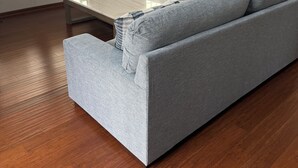 Uma sala de estar com sofá cinzento, uma mesa de centro e chão de madeira.