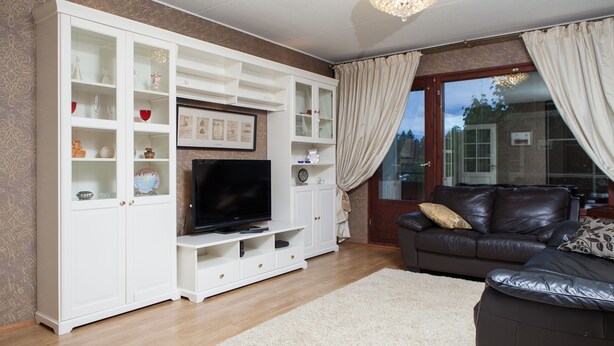 A living room with a white entertainment unit, a flat-screen TV, a brown leather sofa, and a large window with curtains. - Feel yourself at  Three Bears appartment :) (Kotka)