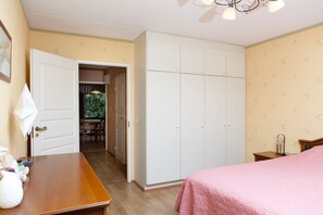 Un dormitorio con un aparador de madera, una cama con edredón rosa, un armario blanco y una mesita de noche pequeña.