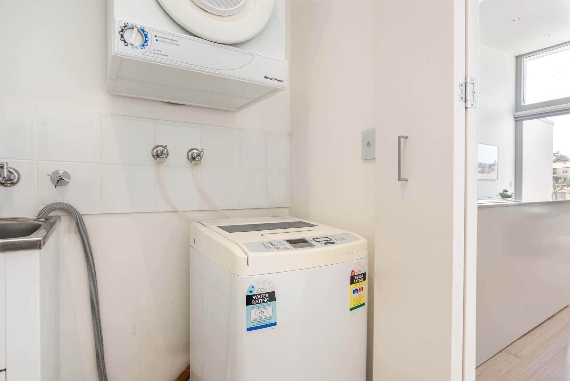 A compact, modern bathroom with a built-in washer and dryer, a wall-mounted heater, and a visible water rating label.