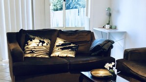 Ein Wohnzimmer mit einem braunen Sofa, einem Glastisch und einem weißen Beistelltisch mit einer Lampe.