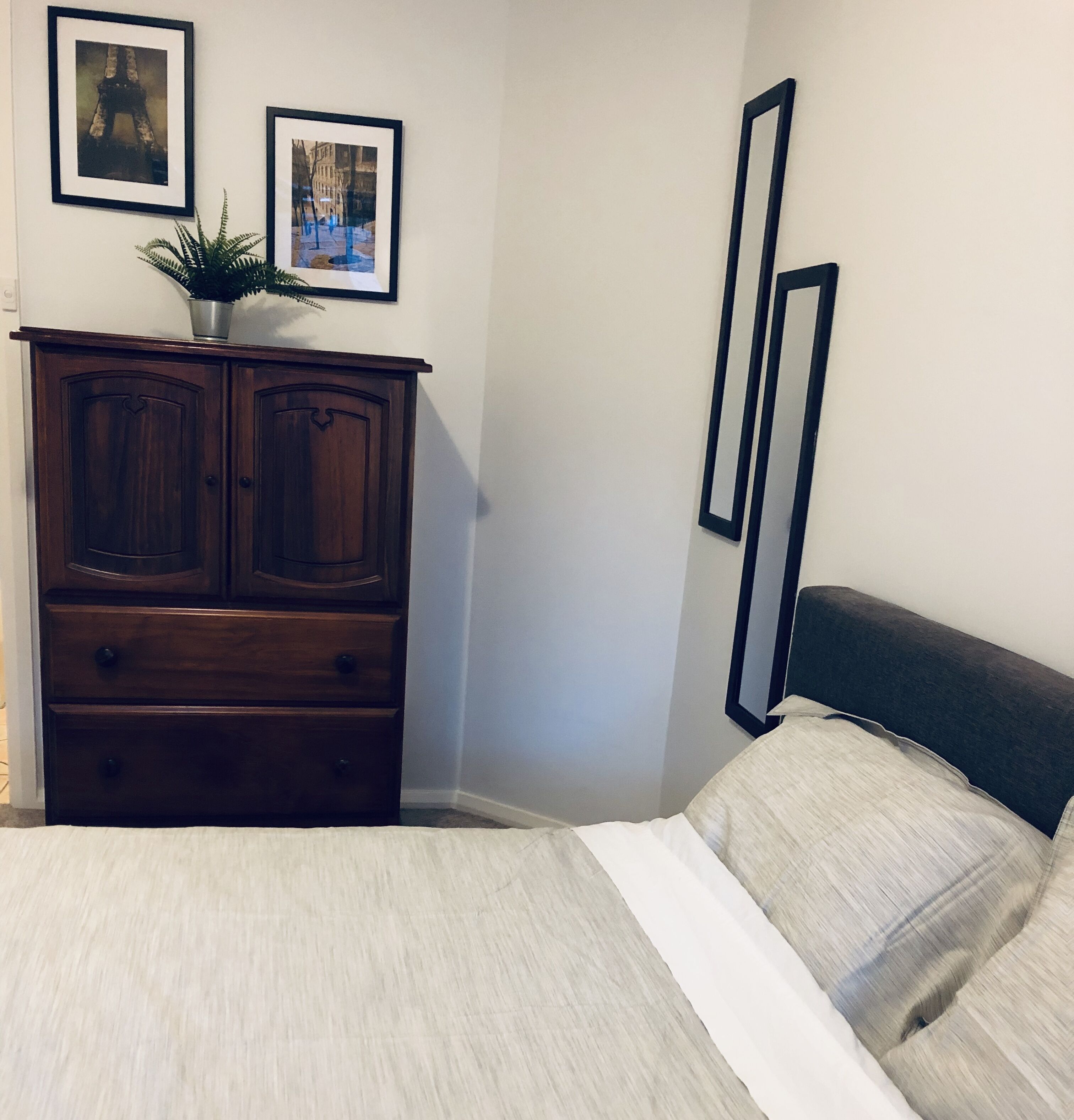A bedroom with a bed, a wooden dresser, and two framed pictures on the wall.