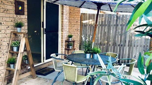Eine Terrasse mit rundem Tisch und Stühlen, eine Holzleiter mit Blumentöpfen und ein Holzzaun im Hintergrund.