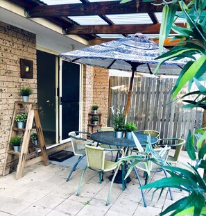 Une terrasse avec une table ronde et des chaises, une échelle en bois ornée de plantes en pot et, au fond, une clôture en bois.