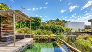 En vacker utomhuspool med en träbrygga och en pergola, omgiven av frodig grönska och ett litet vattenfall.