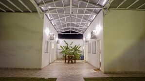 Uma galeria coberta com piso de azulejos, ladeada por paredes e dois aparelhos de ar condicionado.