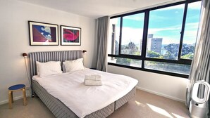 Un dormitorio con cama, una silla, un calentador y una ventana con vistas a la ciudad.
