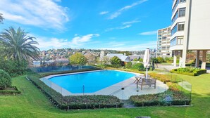 Una piscina rodeada de un jardín cuidado, con vistas a un paisaje urbano de fondo.