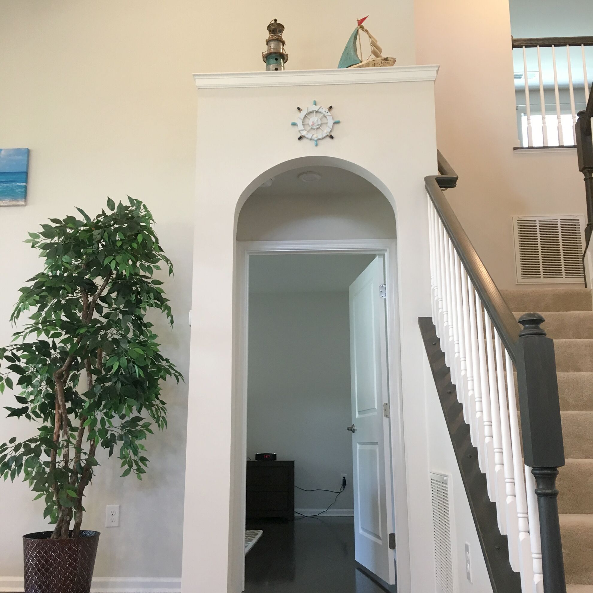 A hallway with a white door, a potted plant, a clock, and a staircase with a railing.