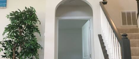 A hallway with a white door, a potted plant, a clock, and a staircase with a railing.