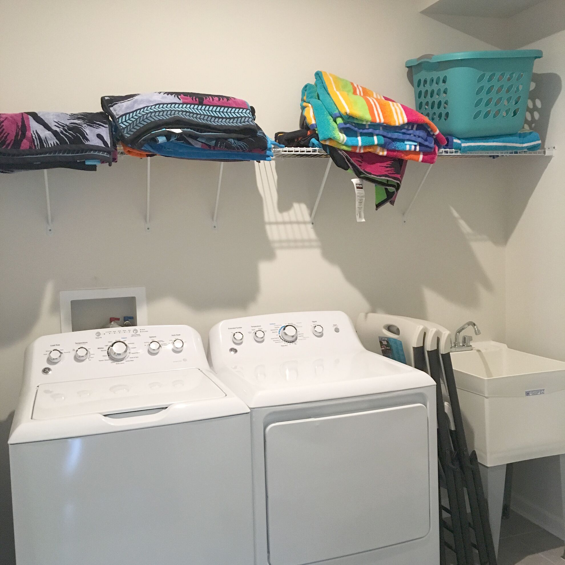 A laundry area with two stacked washing machines and a white sink.