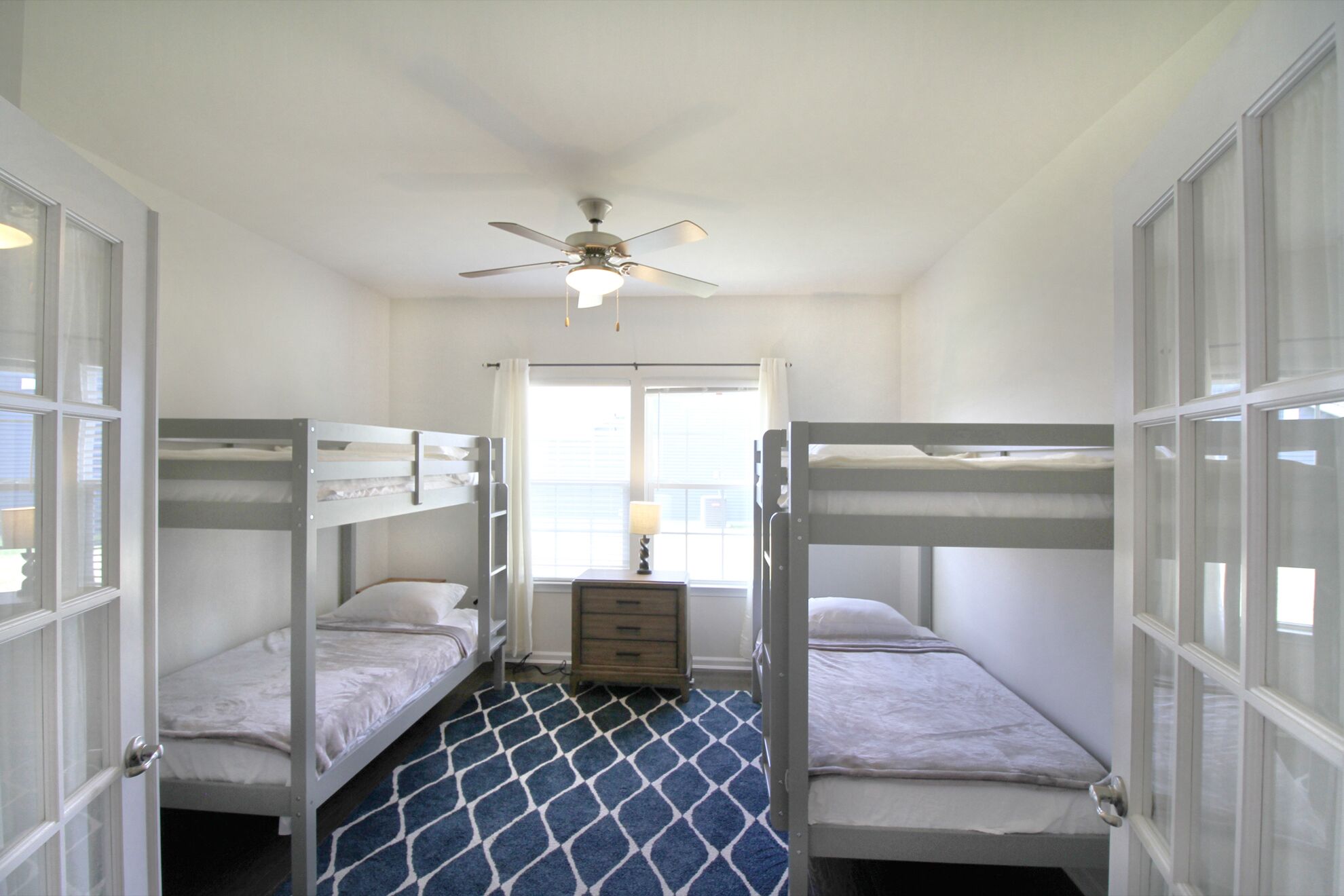 A room with bunk beds, a ceiling fan, a window with curtains, and a dresser.