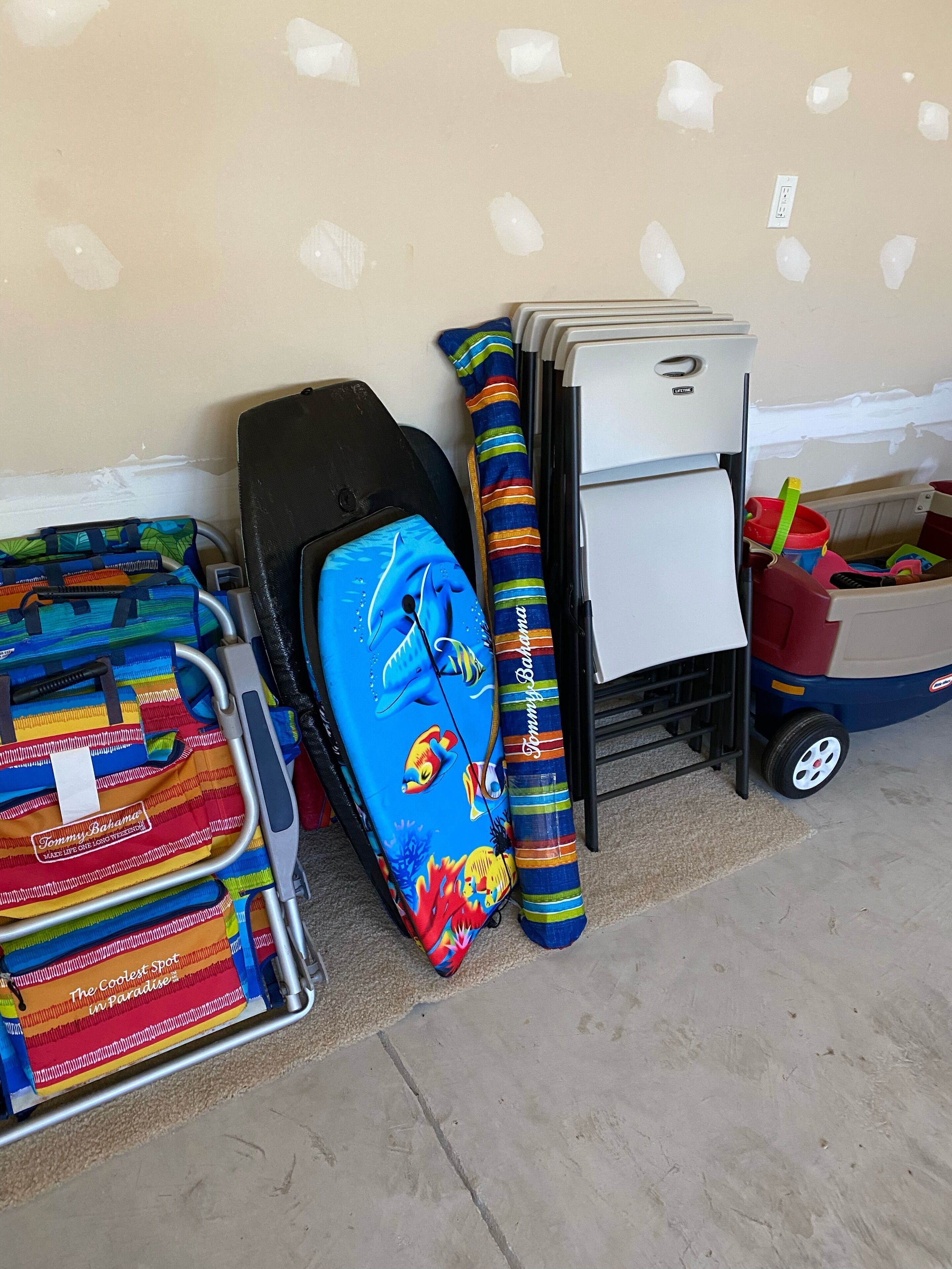 A storage area with various items including a suitcase, a stroller, and a cart with a red container.