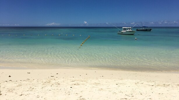 Una playa con agua turquesa cristalina, una orilla arenosa y dos barcos anclados cerca de la orilla.