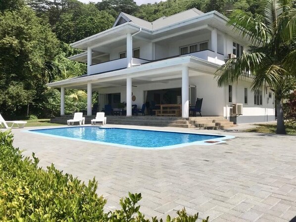 Ein zweistöckiges Haus mit Swimmingpool, weißer Fassade und überdachter Terrasse.