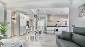 Una cocina moderna con armarios blancos, un comedor con mesa de vidrio y un sofá gris.
