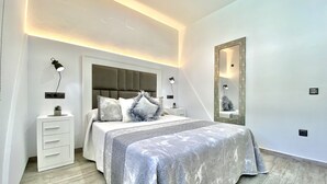 Un dormitorio moderno con cama, mesitas de noche, un espejo e iluminación en la pared.