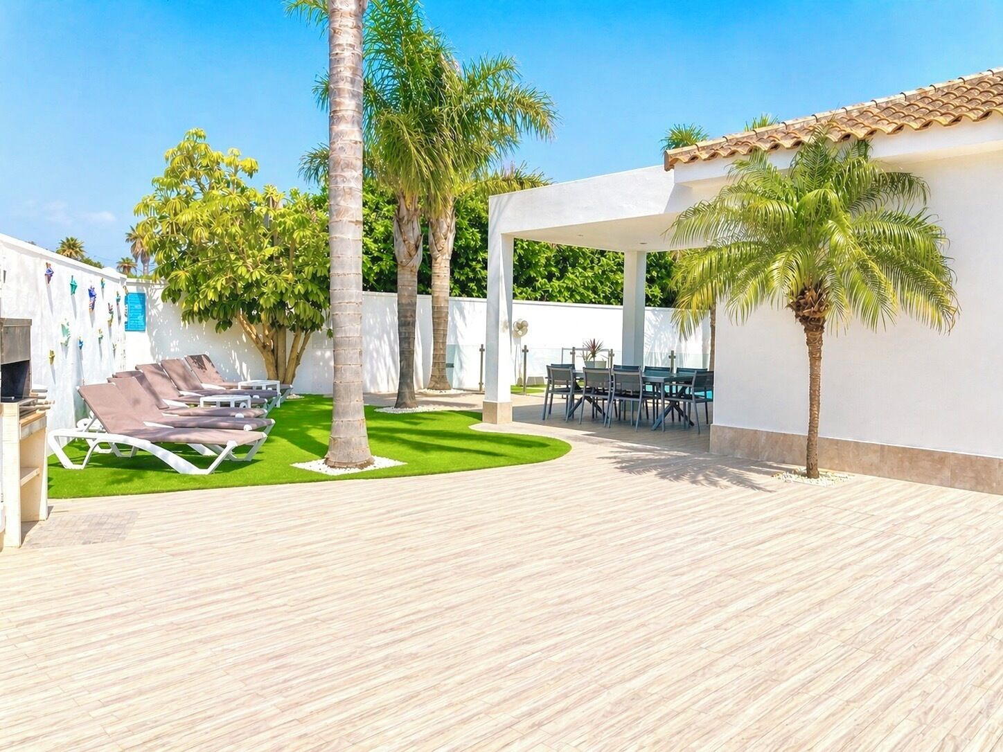 Une terrasse avec des chaises longues, une table à manger et des palmiers.