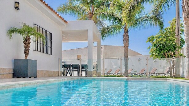 Una piscina con agua cristalina, rodeada de sillas de descanso y palmeras.