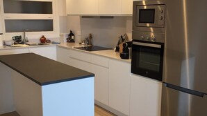 A modern kitchen with white cabinetry, a stainless steel refrigerator, a built-in oven, and a microwave. - Port bo's treasure  (Calella de Palafrugell)