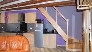 Une cuisine moderne avec des meubles en bois, un réfrigérateur en acier inoxydable et un four à micro-ondes. Un escalier en bois mène à un autre niveau.