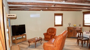 Un salon comprenant un téléviseur, un canapé en cuir, un fauteuil, une table basse en bois et un coin repas avec une table et des chaises.