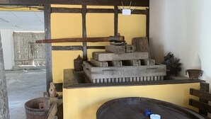 Un intérieur rustique avec des poutres en bois, un mur jaune et une table centrale agrémentée de barils et d’un marteau.
