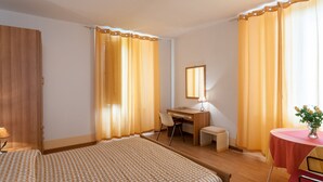 Ein Hotelzimmer mit Bett, Schreibtisch, Stuhl und einem kleinen Tisch mit Blumenvase.
