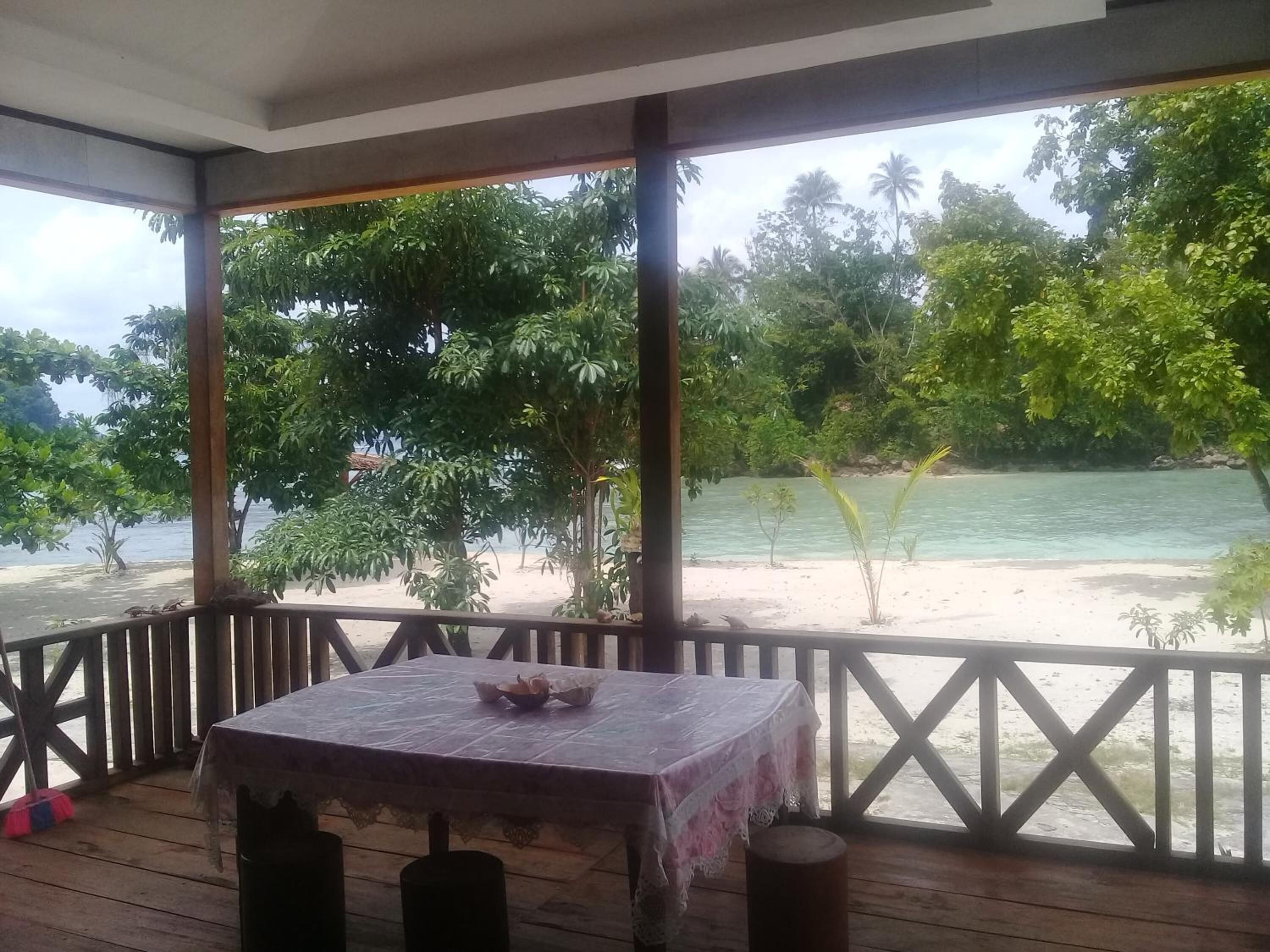 A covered outdoor area with a table and chairs, overlooking a beach and turquoise waters.
