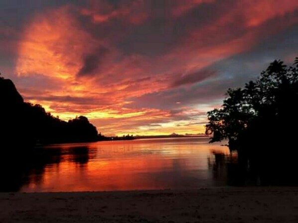 A sunset over a calm lake with a silhouette of a mountain range in the background.