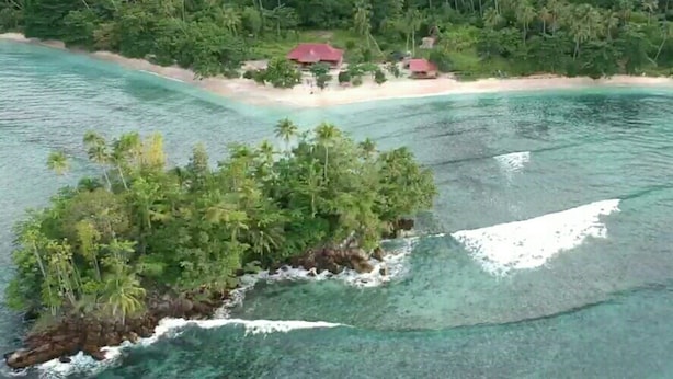 Ett flygbildsbild av en tropisk ö med kristallklart turkost vatten, en liten strand och tät vegetation.