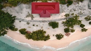 Ett flygbildsbild av en strand med en röd byggnad, kristallklart turkost vatten och här och var utspridd vegetation.