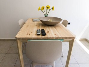 A dining table with a bowl of flowers, two remote controls, and a chair.
