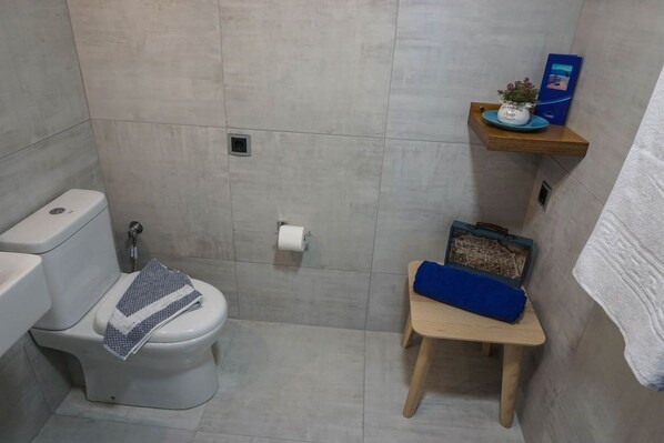 Un baño con inodoro, ducha y un taburete de madera con una toalla.