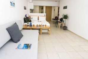 A modern hotel room with a sofa, a small table, a bed, and a dining area with chairs.