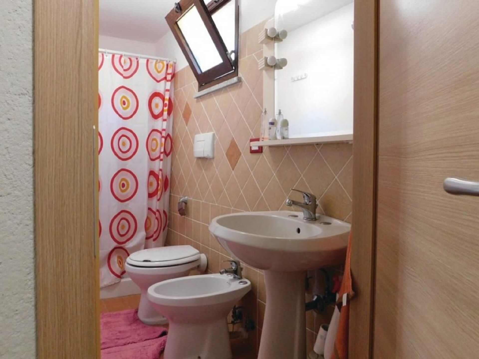 Baño con dos inodoros, un lavamanos y una cortina de ducha con diseño circular.